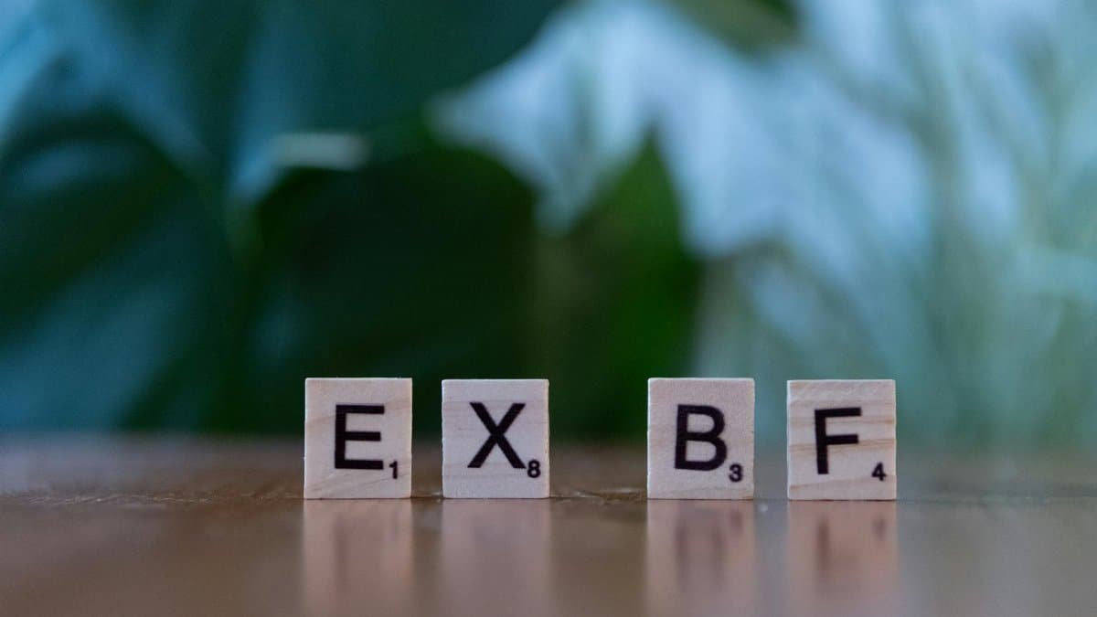 Close-up of Scrabble tiles spelling 'EXBF' on a wooden table with blurred background.