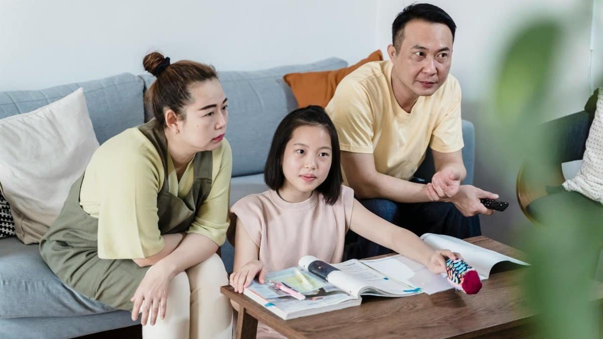 A family of three spending quality time indoors, seated on a couch with books and a remote.