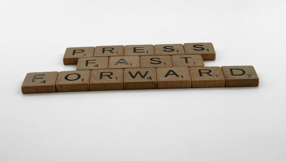 A motivational phrase 'Press Fast Forward' spelled with Scrabble pieces on a white background.