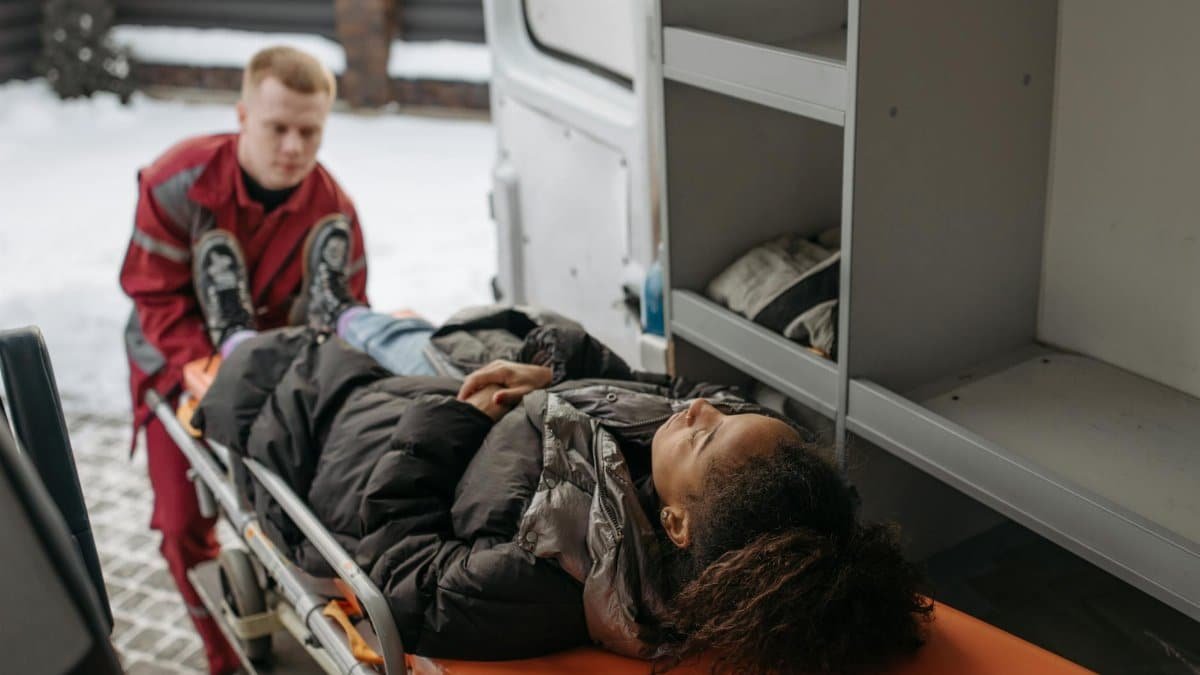 Emergency medical technicians assisting a patient onto a stretcher and into an ambulance.