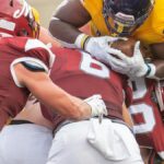 A dynamic scene of American football players in a mid-game tackle during a competitive match.