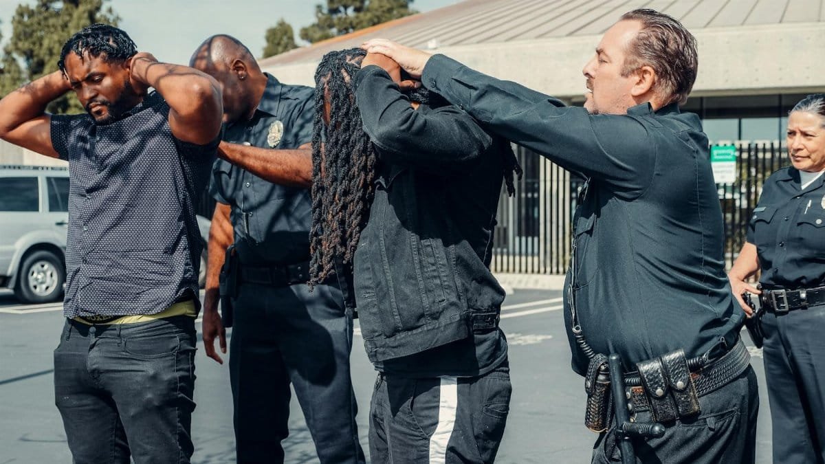 Law enforcement officers performing a pat-down on two individuals in an urban setting.