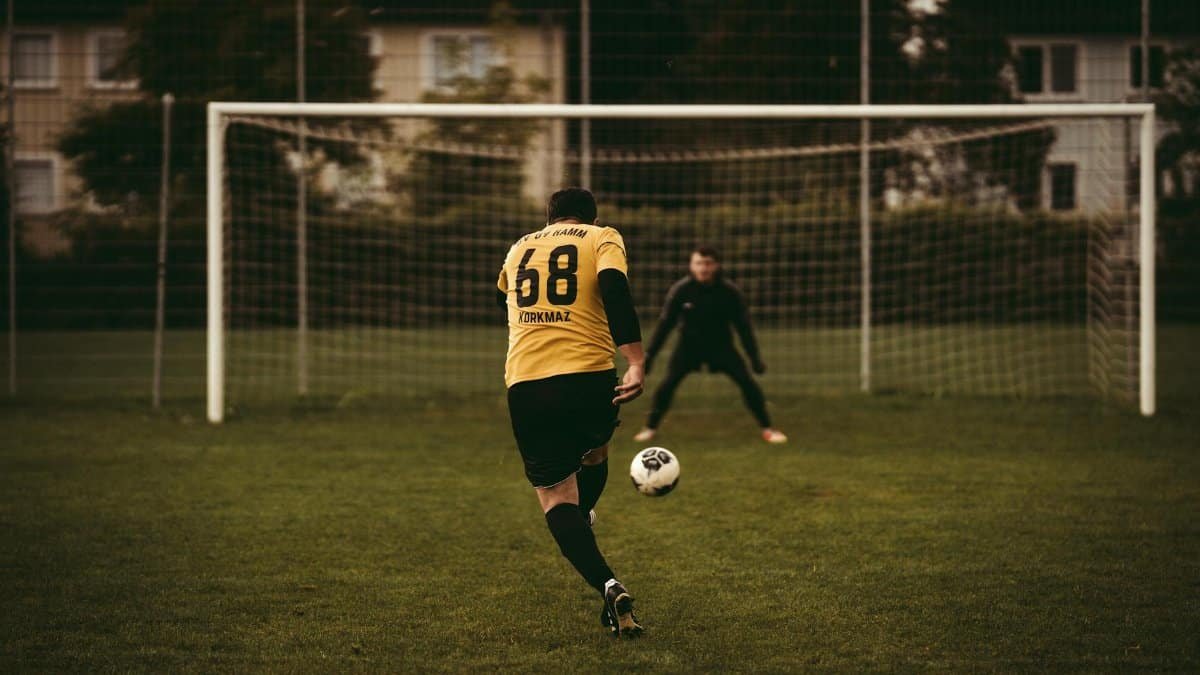 A soccer player takes a decisive penalty kick aiming to score against the goalkeeper.