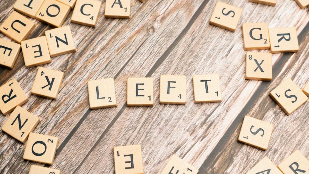 Wooden Scrabble tiles spelling 'LEFT' on a rustic wooden floor, surrounded by scattered tiles.