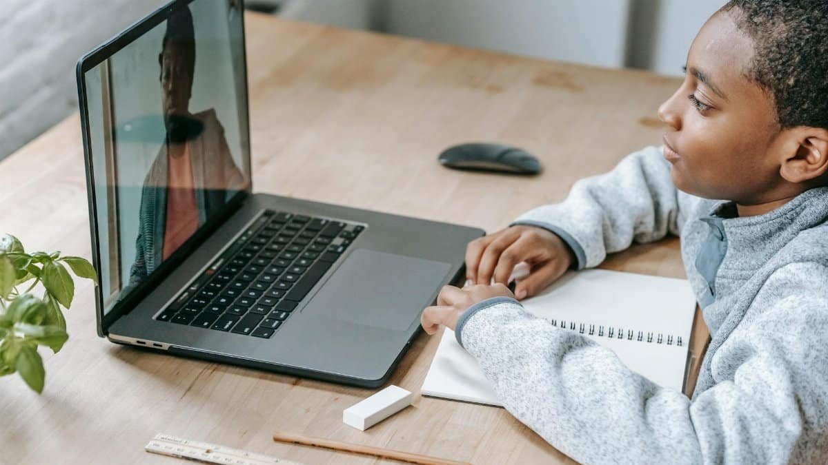 From above side view of crop African American schoolchild watching netbook with speaking female teacher during distance learning at table