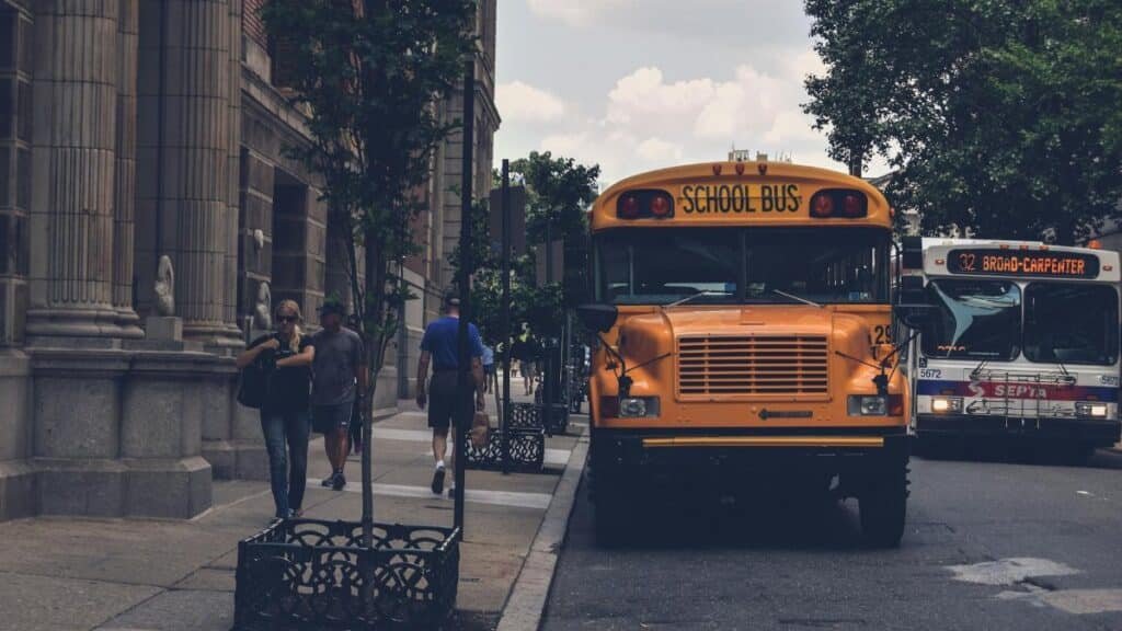 A school bus parked on a city street with pedestrians and a SEPTA bus in Philadelphia.
