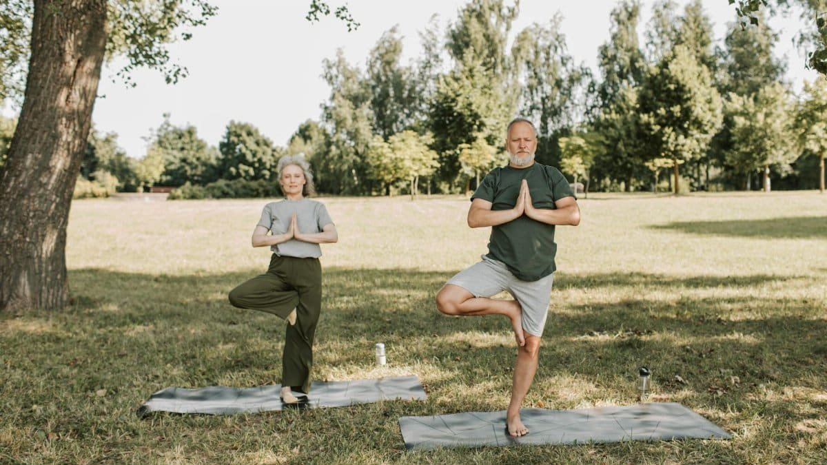 An elderly couple doing yoga in a serene park setting, promoting a healthy lifestyle.