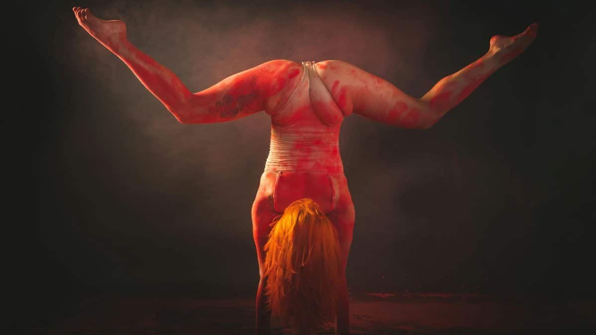A contemporary dancer performs an artistic handstand pose with colored powder accentuating movement.