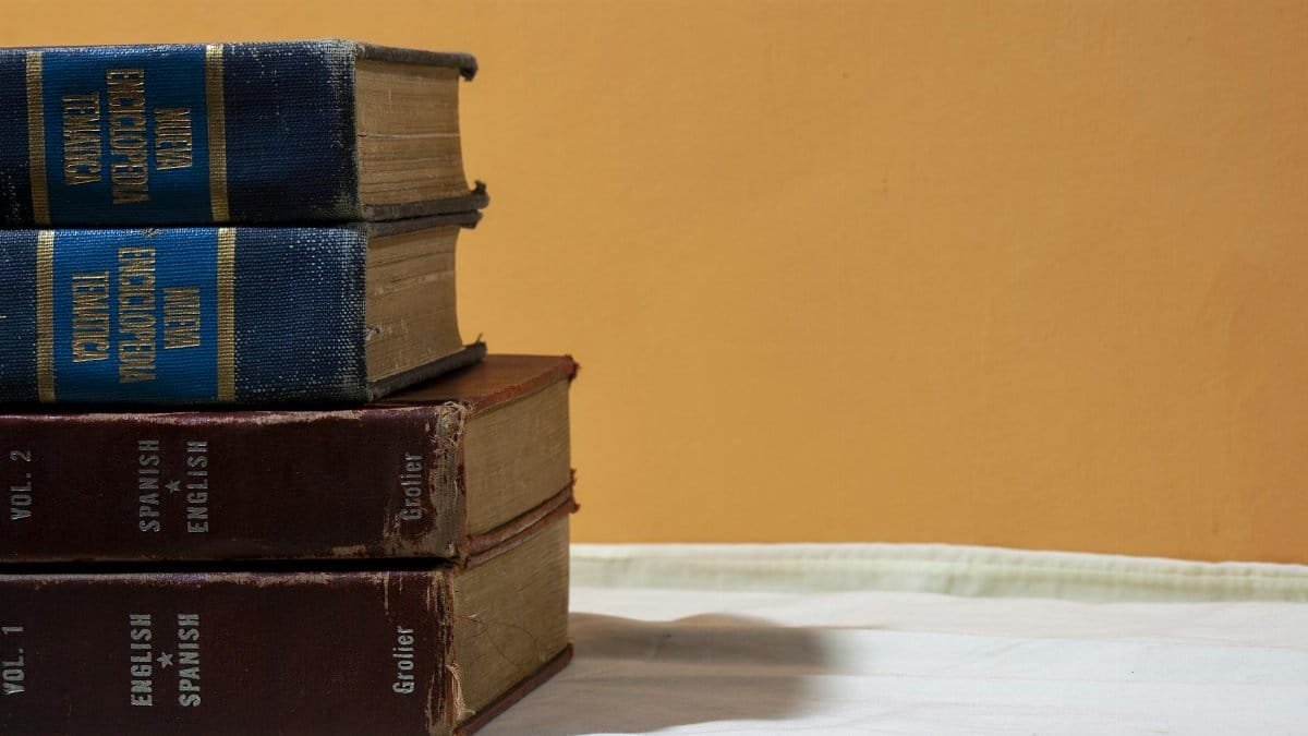 A close-up of vintage English-Spanish dictionaries stacked on a table against a warm backdrop.