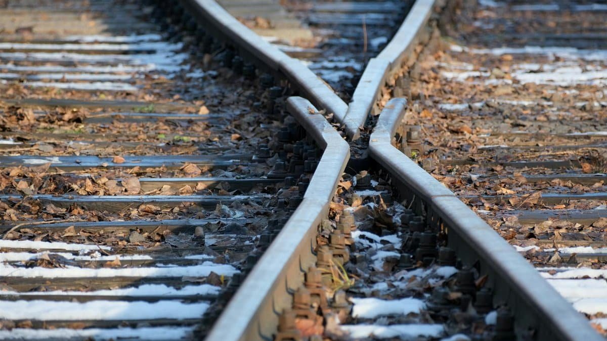 Close-up of converging railroad tracks with fallen autumn leaves and patches of snow.