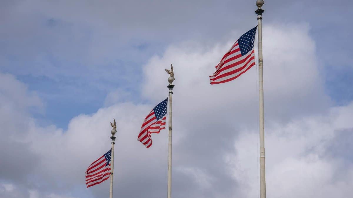 Three American flags waving against a backdrop of fluffy clouds, symbolizing national pride.