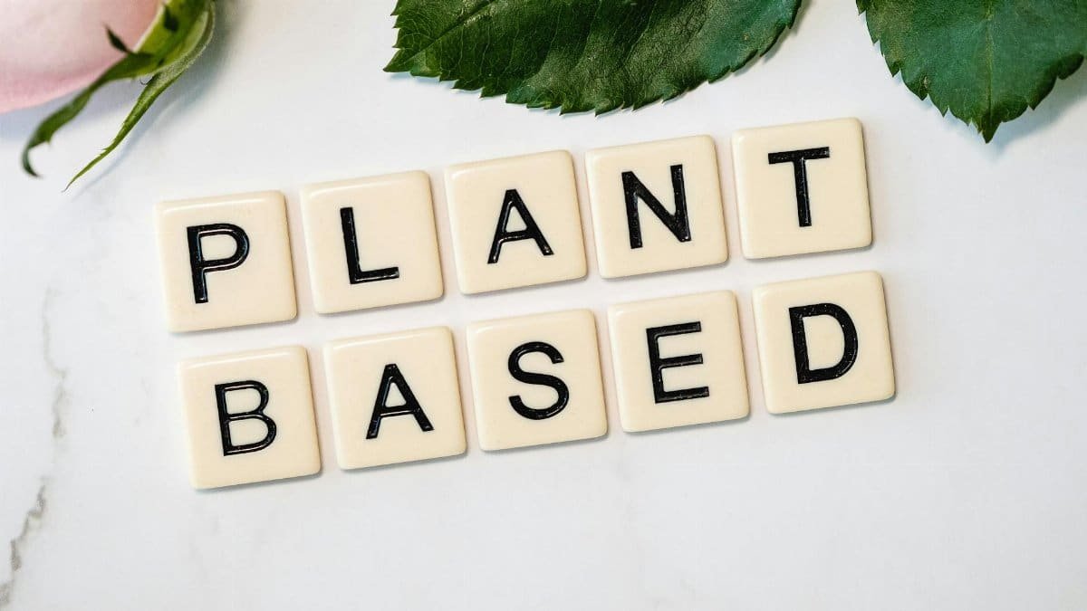 Scrabble tiles spelling 'Plant Based' surrounded by green leaves, promoting a vegan lifestyle.