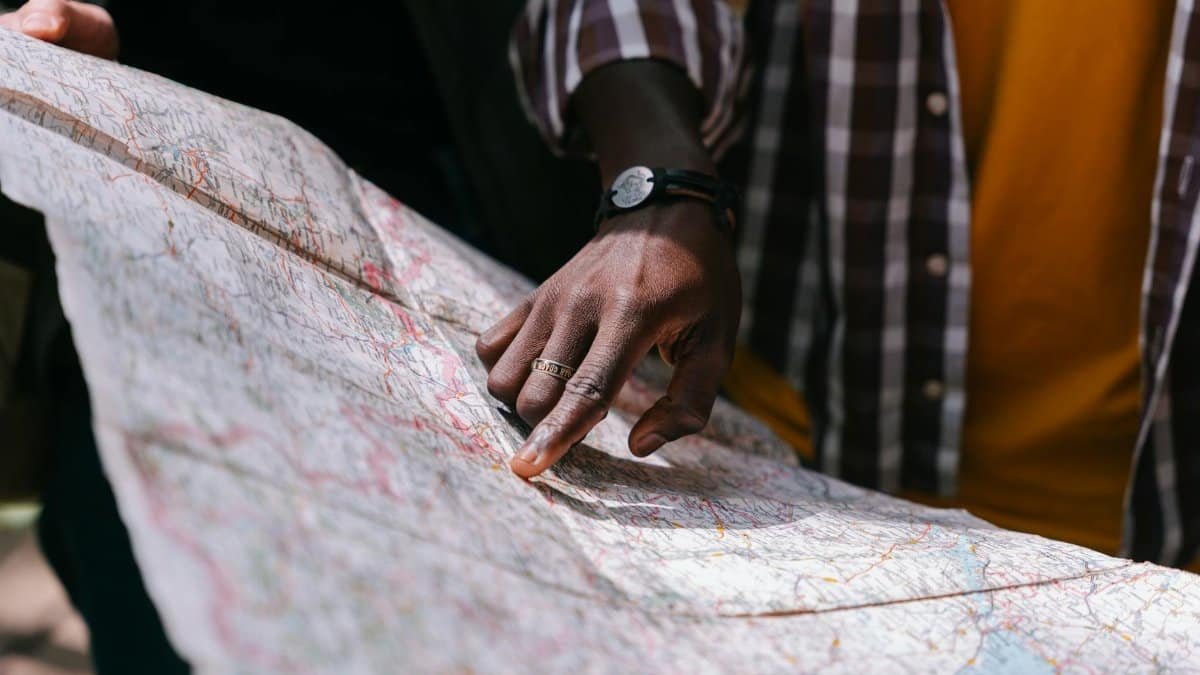 Close-up of a hand pointing at a detailed map, outdoors, wearing a striped shirt.