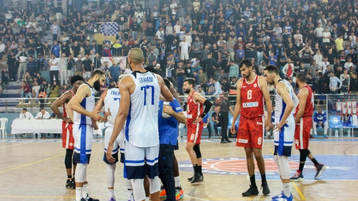 Basketball players in action during a competitive match with a full stadium crowd.