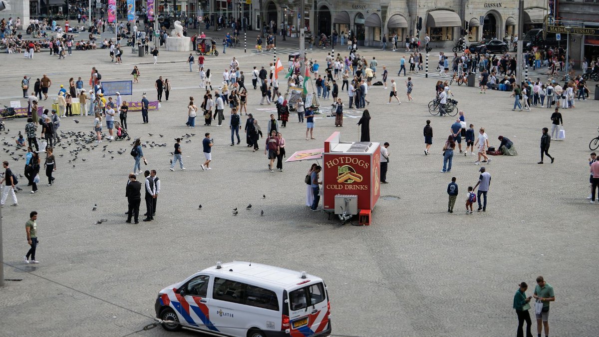 Busy city square with people enjoying a sunny day and street vendors.