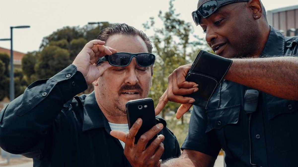 Two police officers analyzing information on a smartphone outdoors.