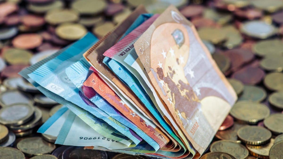 A stack of euro banknotes and scattered coins symbolize wealth and finance.