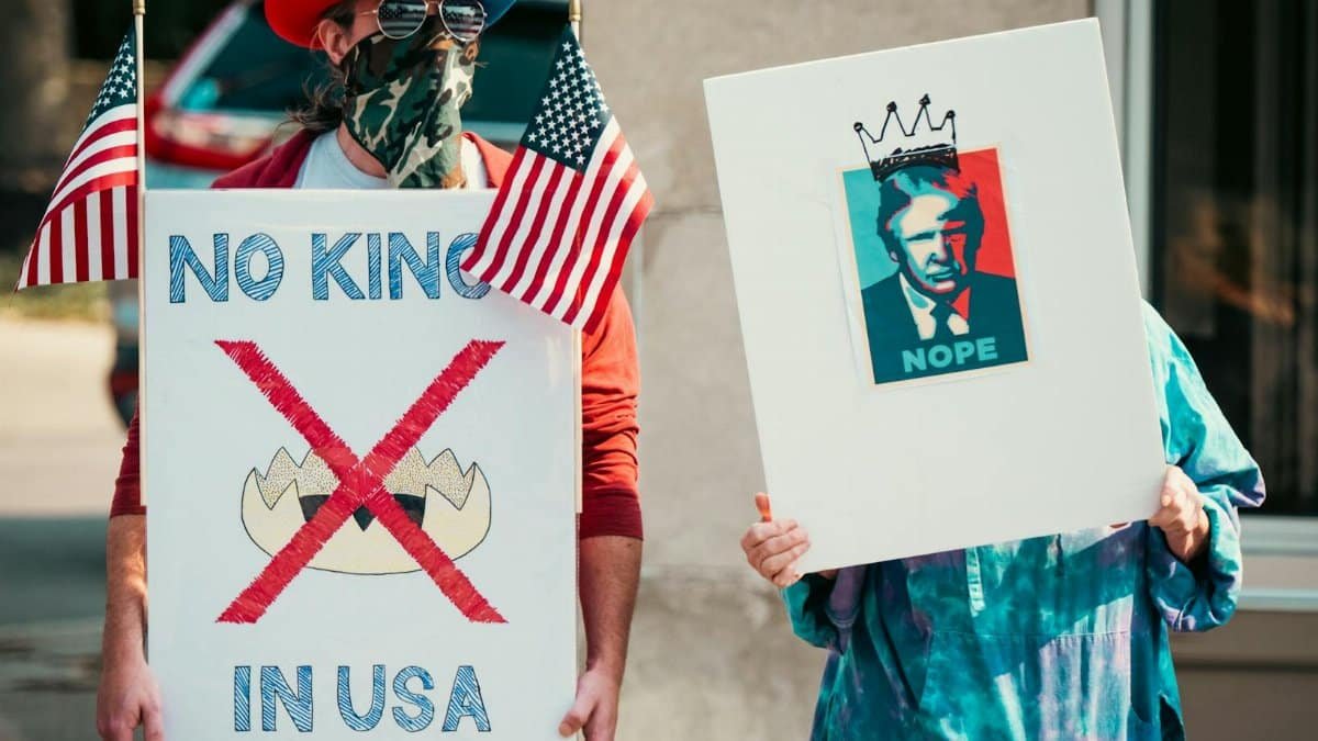 Two protesters displaying political signs during a demonstration with US flags.
