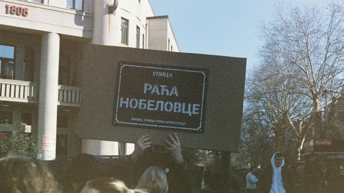Demonstrators holding a sign during a peaceful protest in a city with a historical building.