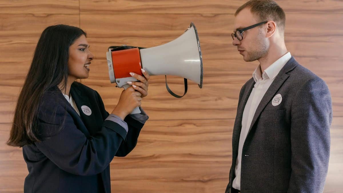 A woman using a megaphone to confront a man in a suit indoors, symbolizing political debate.