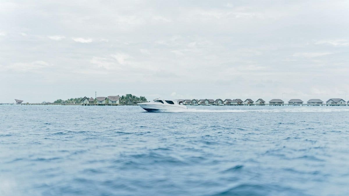 Tranquil scene of a speedboat cruising past overwater villas in the Maldives, under a serene sky.