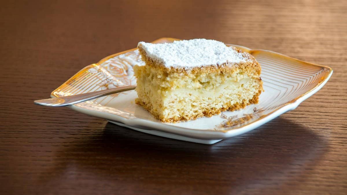 Yummy slice of vanilla cake with powdered sugar on an ornate plate, perfect for dessert lovers.