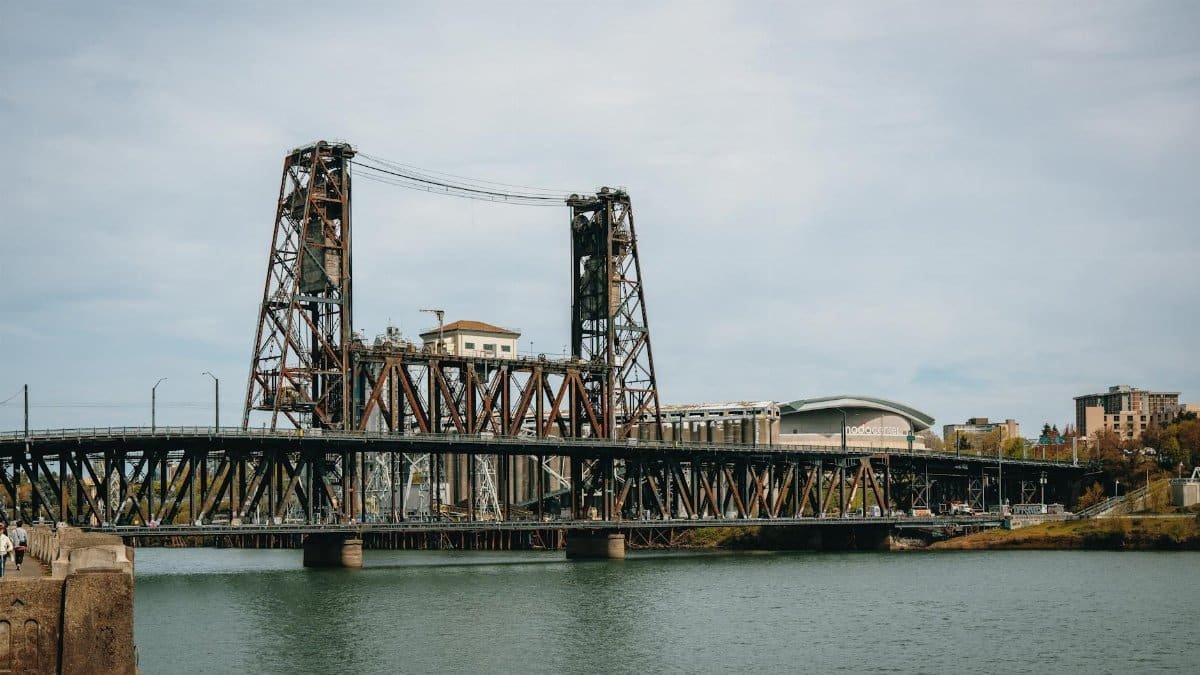 View of Steel Bridge in Portland, Oregon with cityscape and river in the foreground.