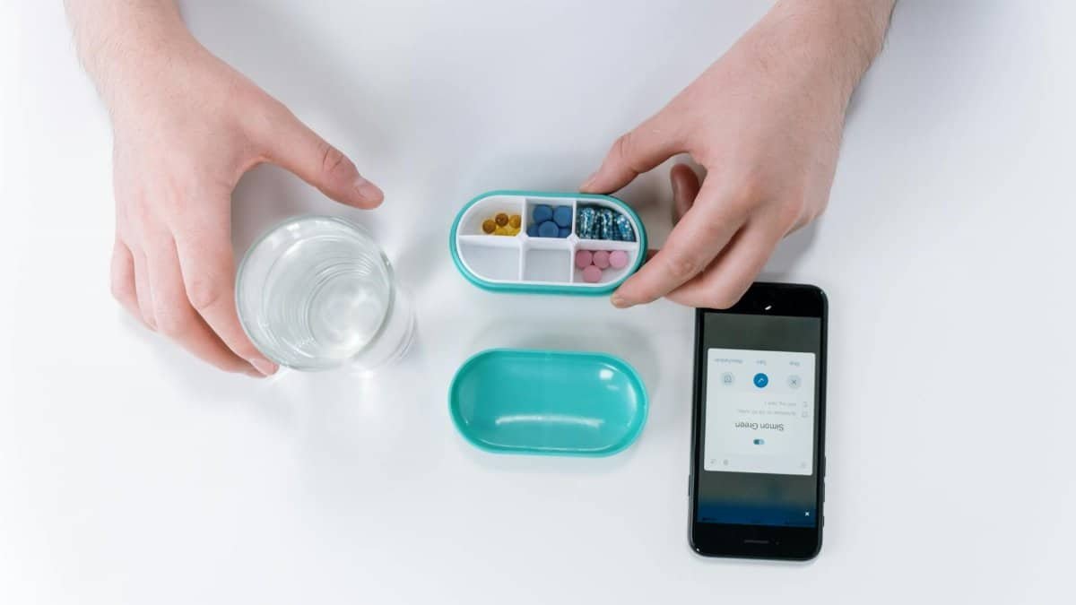 Overhead view of hands using a smartphone app and pill organizer for medication management.