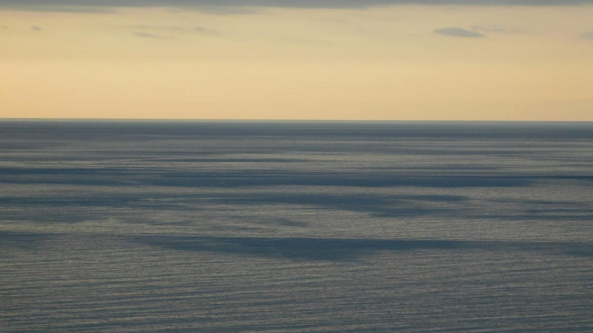 Tranquil view of the calm ocean meeting the horizon with a cloudy sky above.