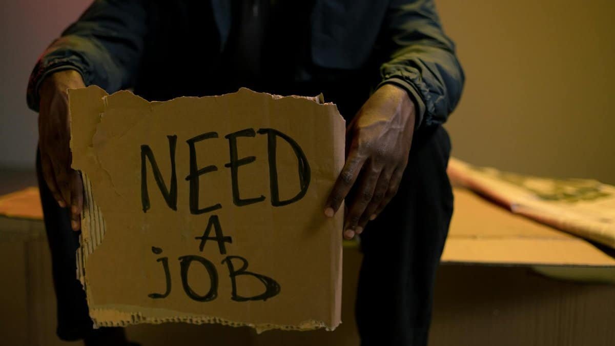 A man holding a cardboard sign reading 'Need a Job', symbolizing unemployment and hardship.
