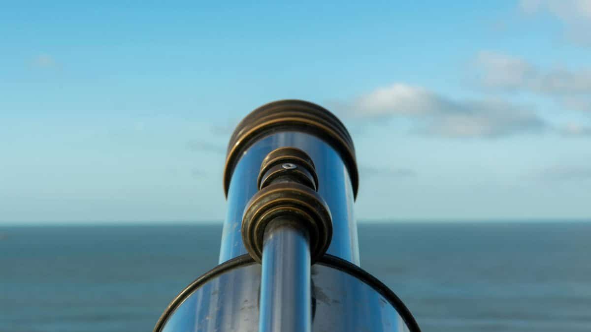 A shiny telescope facing a vast ocean under a clear blue sky, perfect for beachside observation.