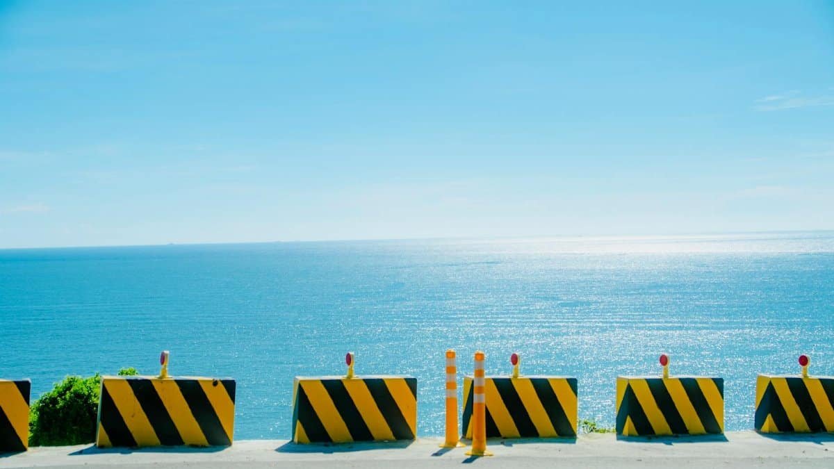 A vibrant view of road barriers against a shimmering seascape under a bright blue sky.