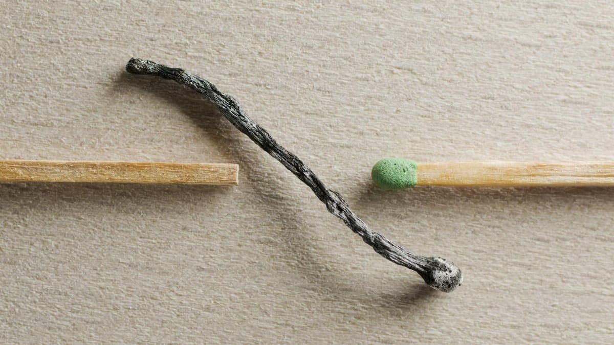 Artistic depiction of contrast between a burnt and unused match on a textured surface.