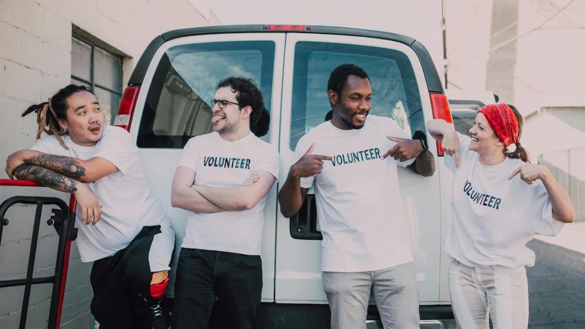 A diverse group of volunteers standing outside a van, smiling and socializing.