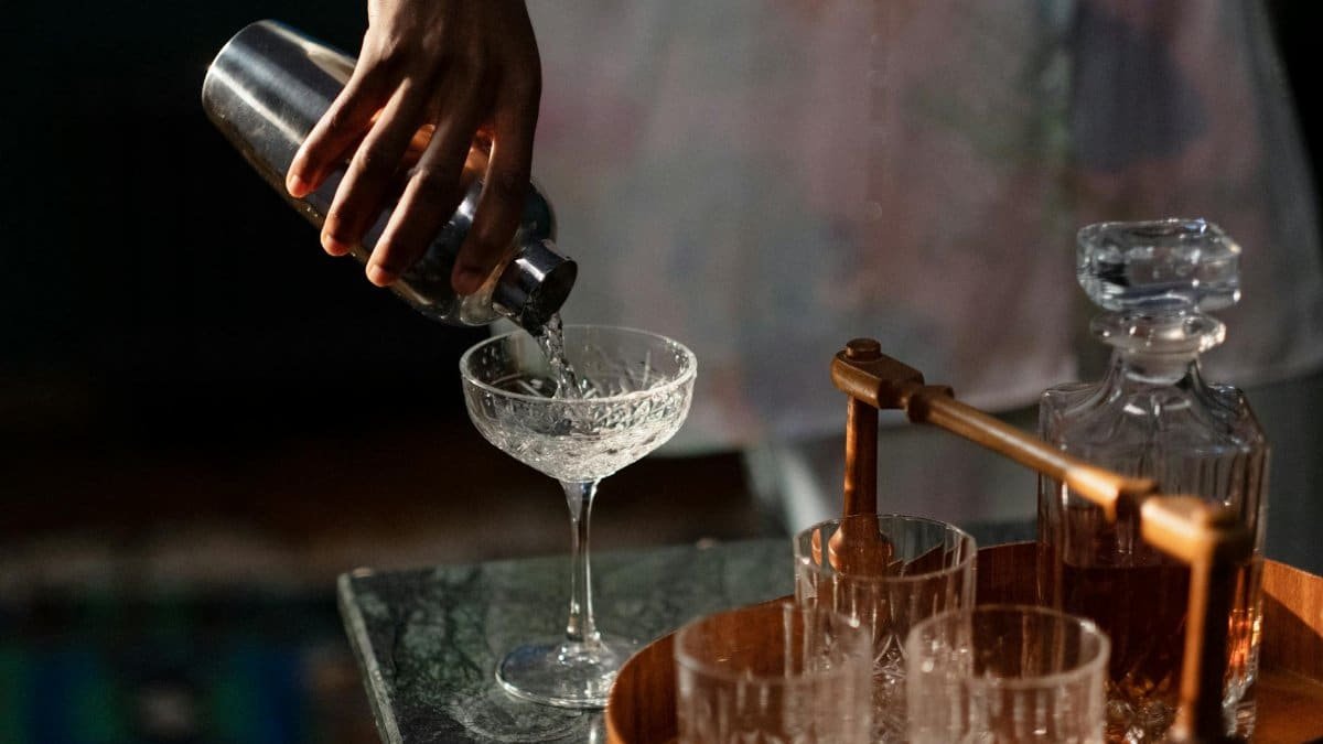 A bartender pours a cocktail into a glass from a shaker, set in a cozy home bar.
