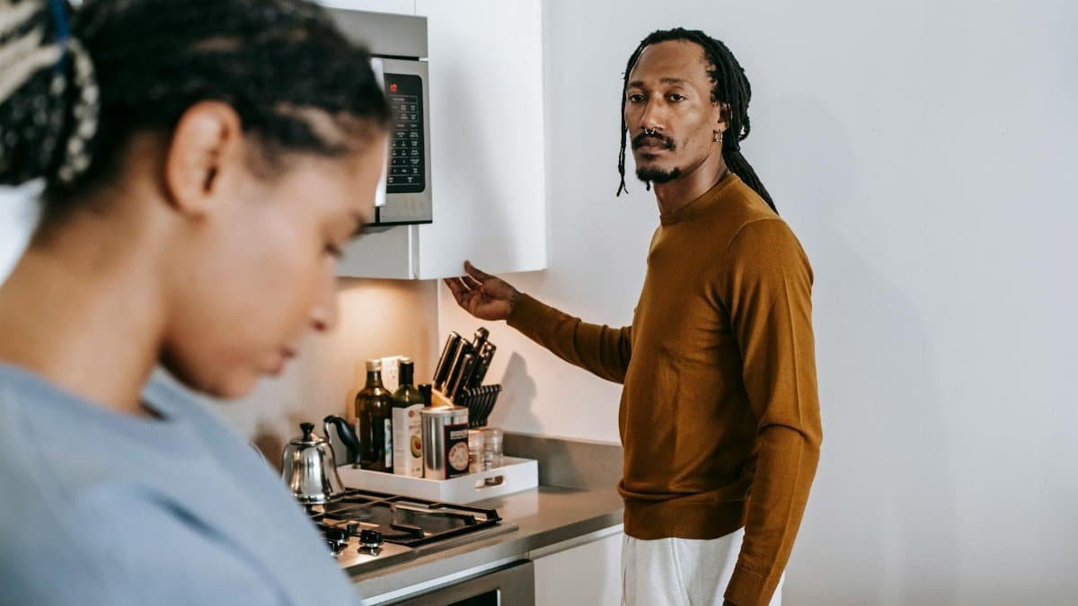 Young black couple in casual outfit standing at kitchen and arguing with each other at home