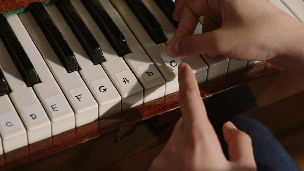 Hands labeling piano keys for beginners. Close-up of a finger pointing at a labeled key.