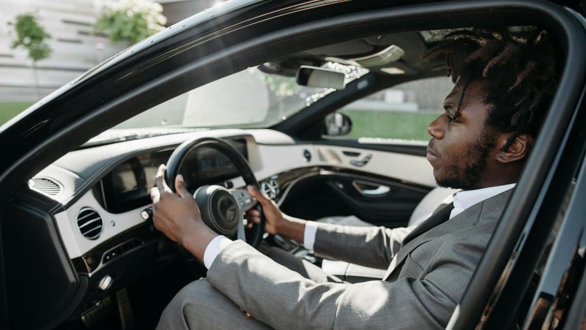 Confident businessman with dreadlocks driving a luxury car in formal attire.
