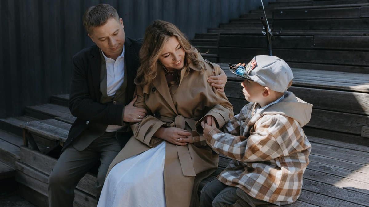 A happy family of three sitting on steps outdoors, sharing moments of affection and joy.