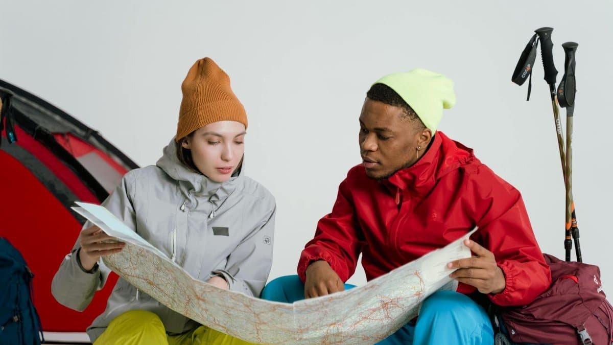 Two adventurers in vibrant winter gear planning a trip with a map indoors.