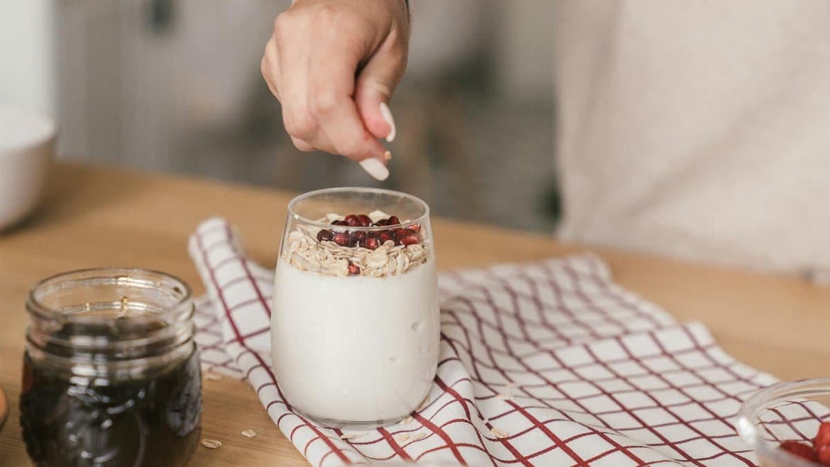 Person preparing yogurt with granola and pomegranate. A nutritious and delicious breakfast idea.