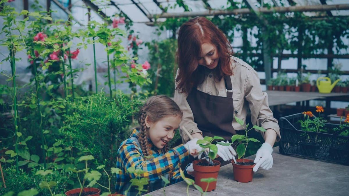 A mother and daughter bonding over gardening in a lush green greenhouse setting.