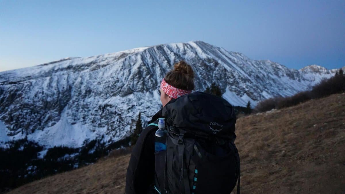 A woman hiker faces a snowy mountain during an outdoor winter hike, capturing the spirit of adventure and exploration.