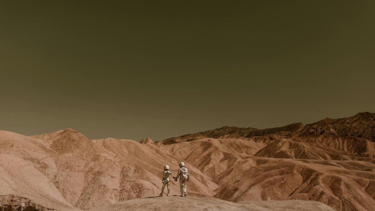Astronauts holding hands, exploring a mars-like desert landscape under a clear sky.