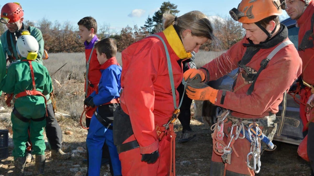Team preparing for a speleology expedition outdoors with helmets and harnesses.