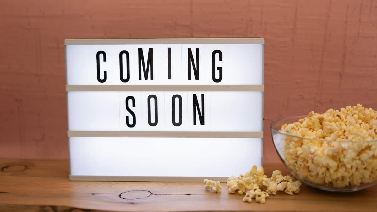 Lightbox sign displaying 'Coming Soon' next to a bowl of popcorn on wooden surface.
