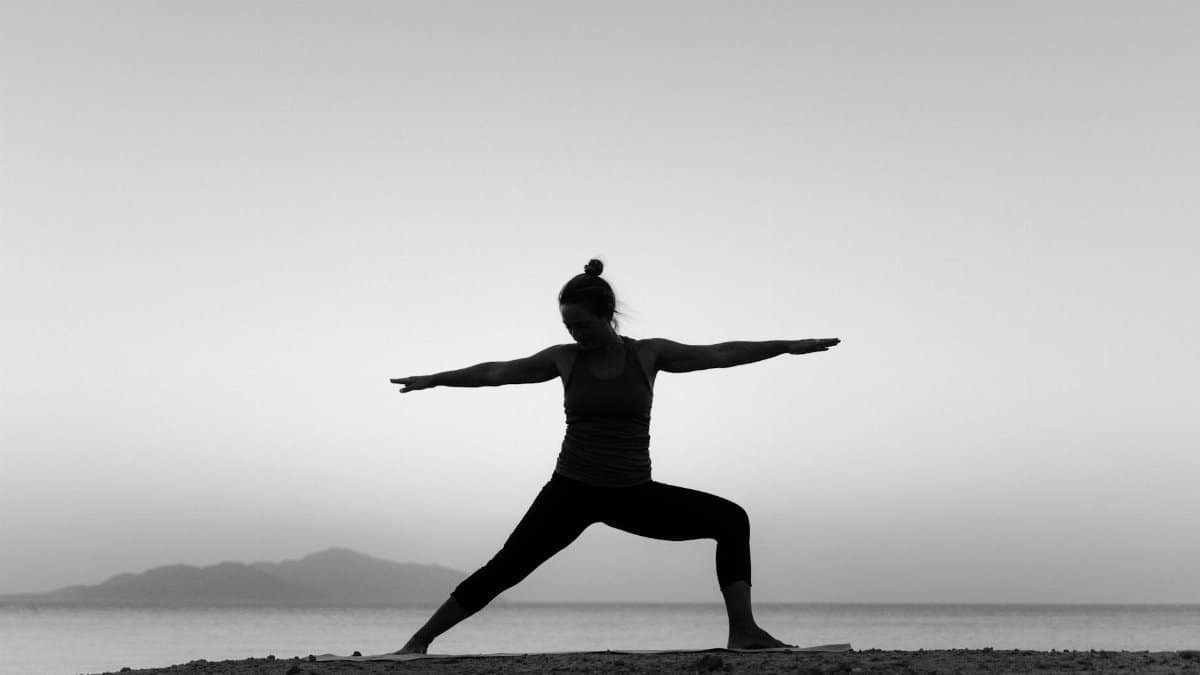 A black and white silhouette of a woman doing yoga on the beach at sunset, embracing a healthy lifestyle.
