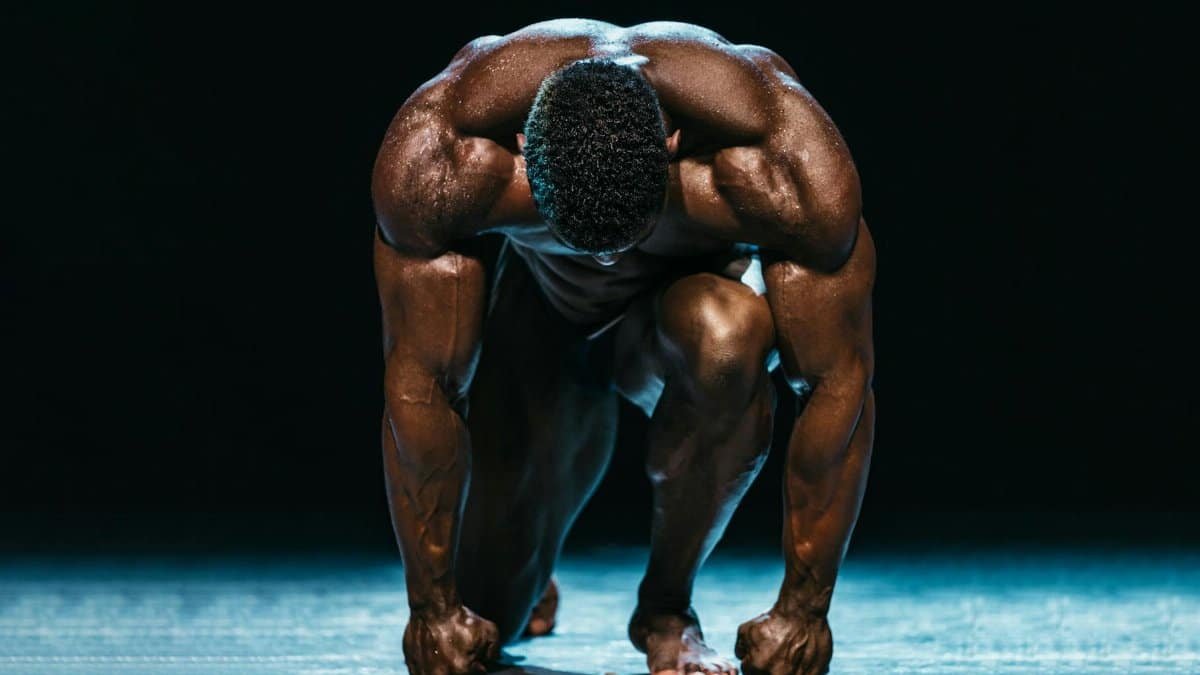 Muscular athlete in a powerful starting position on a dark, dramatic stage.