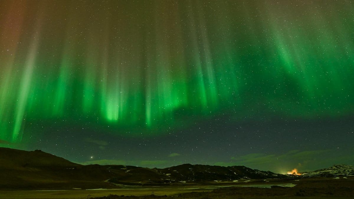 Breathtaking view of Northern Lights dancing over wintery Icelandic terrain at night.