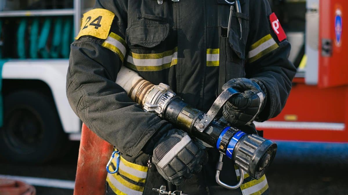 Firefighter in protective gear holding a hose nozzle, ready for action.